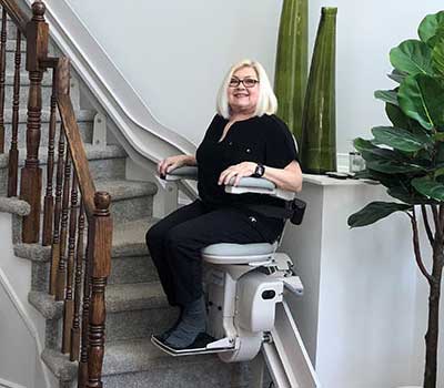Woman riding a stairlift in a home setting.